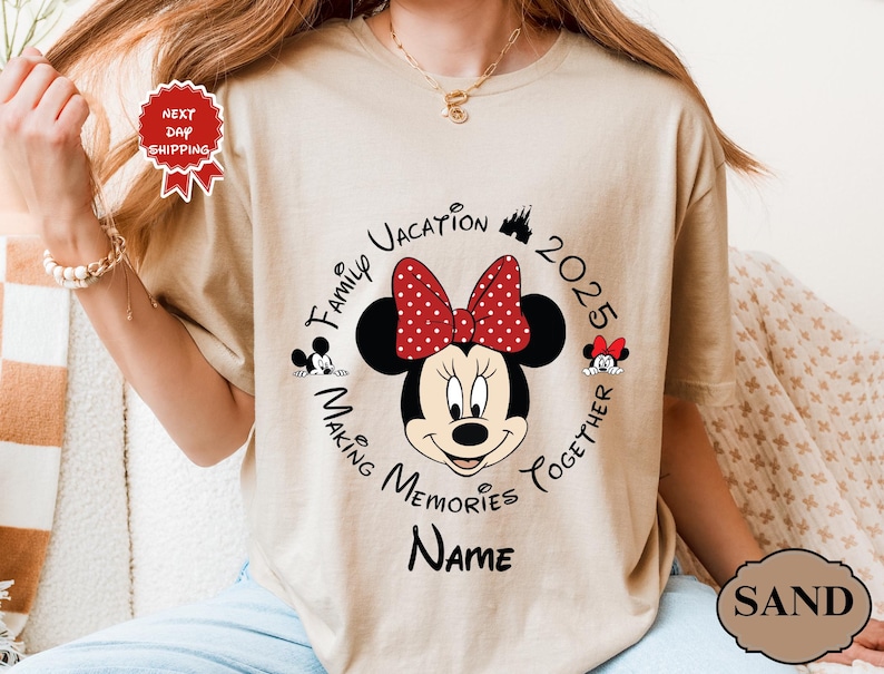 May include: A sand-coloured t-shirt with a Minnie Mouse graphic, sporting a red polka-dot bow. The design includes the text "Family Vacation 2025 Making Memories Together" and space for a name. A "Next Day Shipping" sticker is visible.