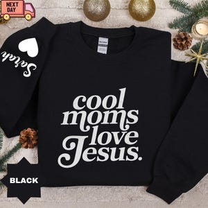 May include: Black sweatshirt with the text "cool moms love Jesus" in white script. The left sleeve has the name "Sarah" in white script with a white heart. The word "BLACK" is at the bottom of the image.