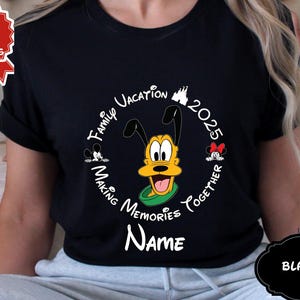 May include: Black t-shirt with a circular design featuring Pluto, Mickey, and Minnie Mouse. The design includes the text "Family Vacation 2025 Making Memories Together" and space for a name. A "Next Day Shipping" sticker is visible.