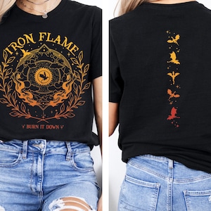 Puede incluir: Camiseta negra con un diseño gráfico de un círculo con llamas y el texto "Iron Flame" y "*Burn it Down*" en la parte delantera. La parte posterior de la camiseta tiene una línea vertical de cinco dragones en diferentes tonos de naranja y rojo.