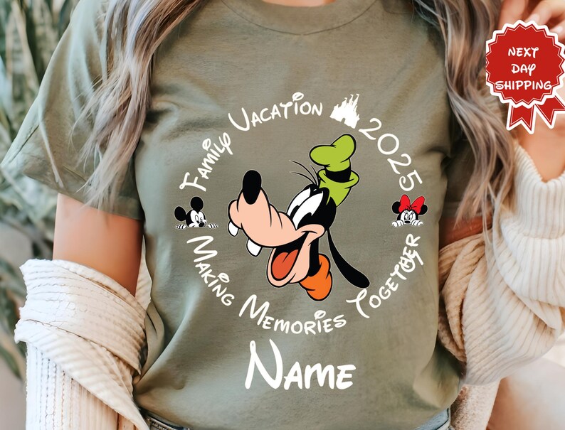 May include: Olive green t-shirt with a cartoon of Goofy and the text "Family Vacation 2025 Making Memories Together". The design includes Mickey and Minnie Mouse. The word "Name" is below the design.