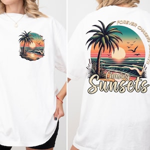 Pu&ograve; includere: T-shirt bianco con un vivace design a tema spiaggia. La parte anteriore presenta una piccola grafica con una palma e un tramonto. Il retro presenta un design pi&ugrave; grande con una palma, onde e il testo "Forever Chasing Sunsets" e "Chasing Sunsets".