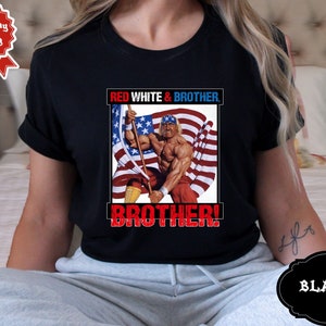 May include: Black t-shirt with a graphic of a wrestler holding an American flag. The text "RED WHITE & BROTHER. BROTHER!" is printed on the shirt.