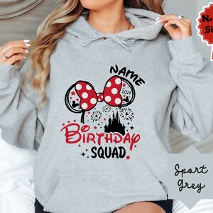 May include: A gray hooded sweatshirt with a black and red graphic design. The graphic features a red bow with white polka dots, a black castle, and the text "NAME 2021 Birthday Squad".