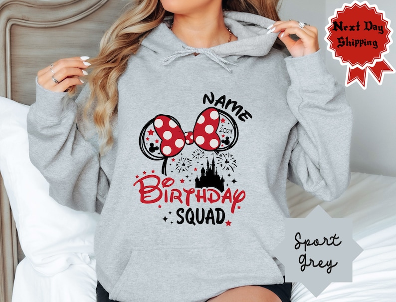May include: A gray hooded sweatshirt with a black and red graphic design. The graphic features a red bow with white polka dots, a black castle, and the text "NAME 2021 Birthday Squad".
