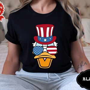 May include: A black t-shirt with a cartoon duck wearing a red, white, and blue Uncle Sam hat and sunglasses. The sunglasses have stars and stripes.
