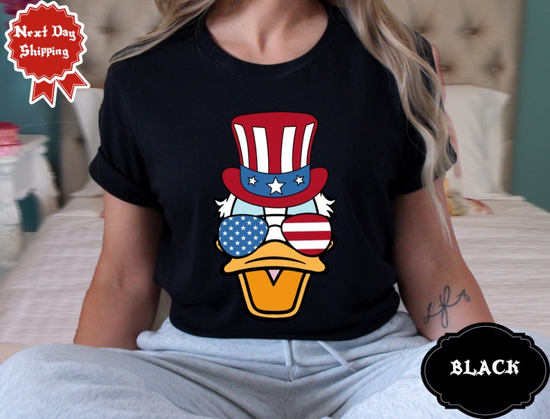 May include: A black t-shirt with a cartoon duck wearing a red, white, and blue Uncle Sam hat and sunglasses. The sunglasses have stars and stripes.