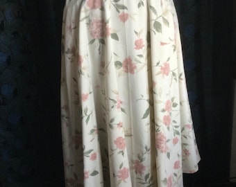 May include: A white skirt with a floral print in shades of pink and green. The skirt is knee-length and has a full, flowing silhouette.