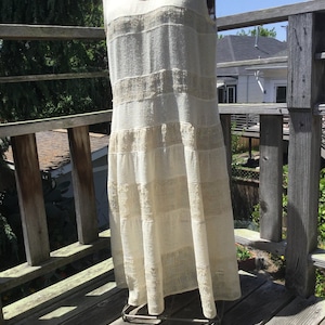 May include: A white sleeveless maxi dress with a textured, crocheted design. The dress has a relaxed fit and a flowing skirt.