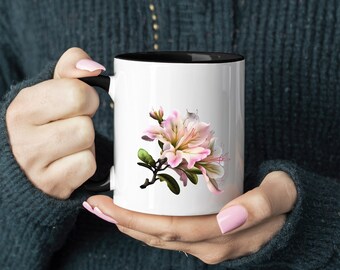 Könnte beinhalten: Eine weiße Keramiktasse mit schwarzem Rand und Henkel zeigt eine rosa und weiße Blume mit grünen Blättern. Die Tasse wird von einer Person gehalten.
