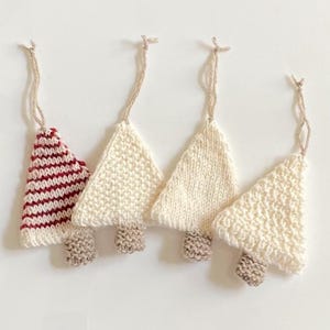 Peut inclure: Quatre décorations de Noël en tricot en forme d'arbre, trois sont blanches et une est rayée rouge et blanche.