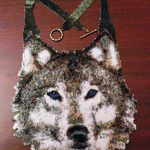 Könnte beinhalten: Eine Perlenkette mit einem Wolfskopf-Design. Das Wolfsgesicht besteht aus kleinen, bunten Perlen und hat ein realistisches Aussehen. Die Kette ist aus schwarzen und grünen Perlen gefertigt und hat einen goldenen Verschluss.