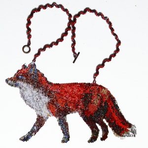 Puede incluir: Un collar de cuentas con forma de zorro con un esquema de color rojo, blanco y negro. El zorro está representado en una pose de caminar con la cola enroscada detrás de él. El collar está hecho con una cadena de color rojo oscuro.
