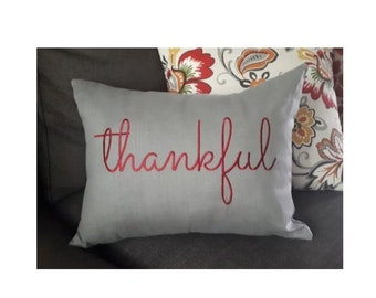 May include: A gray throw pillow with the word "thankful" embroidered in red.