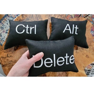 May include: Three black pillow cushions with white embroidered text. The pillows read "Ctrl", "Alt", and "Delete".