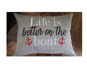 May include: A gray linen pillow with the text "Life is better on the boat" embroidered in black and white. Two red anchors are embroidered on either side of the word "boat".