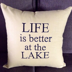 May include: A white throw pillow with the text "LIFE is better at the LAKE" embroidered in navy blue.