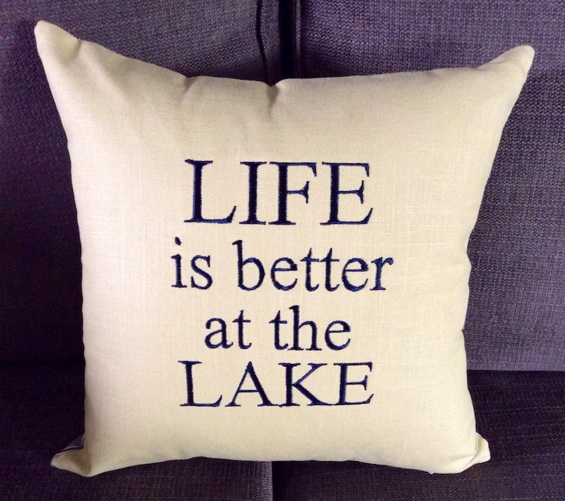 May include: A white throw pillow with the text "LIFE is better at the LAKE" embroidered in navy blue.