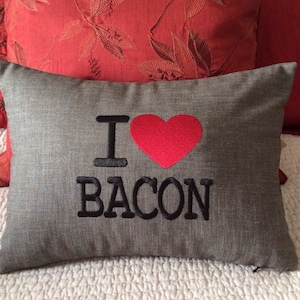 May include: Gray pillow with black embroidered text that reads "I love bacon" and a red heart.