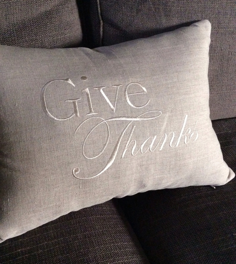 May include: A gray linen throw pillow with white embroidery that reads "Give Thanks".