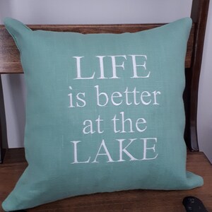 May include: A teal green throw pillow with white text that reads "LIFE is better at the LAKE".