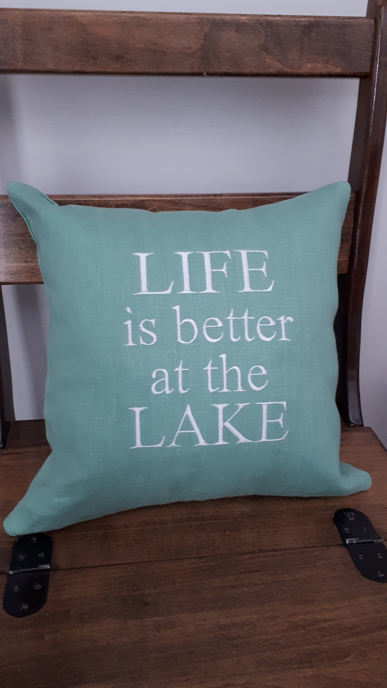 May include: A teal green throw pillow with white text that reads "LIFE is better at the LAKE".