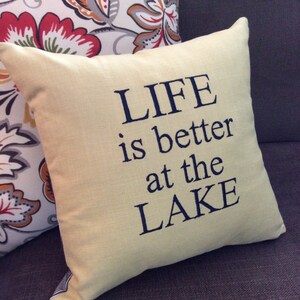 May include: A yellow throw pillow with the text "LIFE is better at the LAKE" embroidered in dark blue thread.