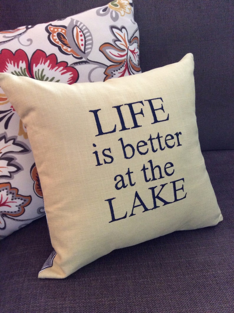 May include: A yellow throw pillow with the text "LIFE is better at the LAKE" embroidered in dark blue thread.