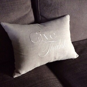May include: A gray throw pillow with the words "Give Thanks" embroidered in white.