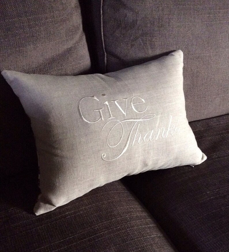 May include: A gray throw pillow with the words "Give Thanks" embroidered in white.