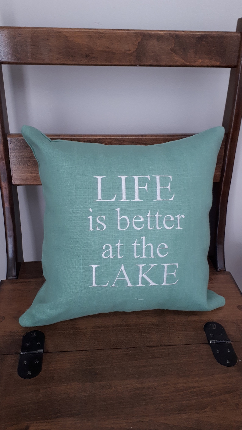 May include: A teal green throw pillow with white text that reads "LIFE is better at the LAKE".
