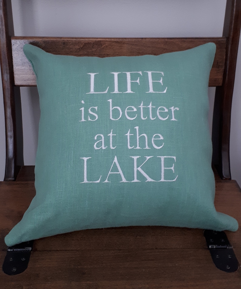 May include: A teal green throw pillow with white embroidered text that reads "LIFE is better at the LAKE".