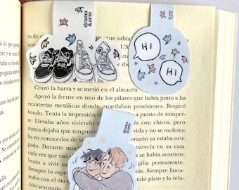 Peut inclure: Deux signets avec des illustrations. Un signet présente une bulle de dialogue bleue avec le mot "HI" en texte blanc. L'autre signet présente une illustration de bande dessinée de deux personnes qui se font un câlin. Le texte "drama & arte" est visible sur le signet.