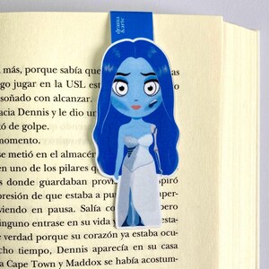 May include: A blue and white bookmark featuring a cartoon illustration of a woman with blue hair and a white dress. The bookmark has the text "drama & arte" printed on it.