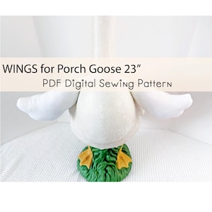 Könnte beinhalten: Ein weißes Plüschgans mit ausgebreiteten Flügeln, vor weißem Hintergrund. Die Gans hat einen grünen Sockel mit gelben Füßen. Der Text auf dem Bild lautet "WINGS for Porch Goose 23" PDF Digital Sewing Pattern."
