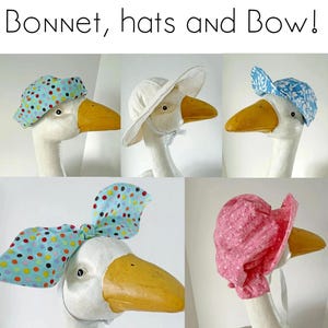 Op de afbeelding: Een assortiment decoratieve ganzenkoppen met verschillende hoeden en een strik. De hoeden omvatten een blauwe stippenmuts, een witte zonnehoed, een blauwe bloemenpet, een grote blauwe stippenstrik en een roze stippenmuts.