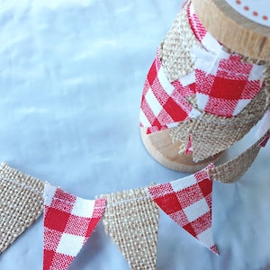 May include: A red and white gingham and burlap banner with triangle flags. The banner is rolled up on a wooden spool.