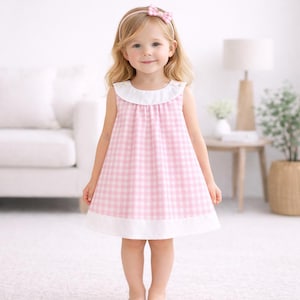 May include: A sleeveless pink and white gingham dress with a white collar and hem. The dress is worn by a young child, who is also wearing a matching pink headband with a bow. The dress is a classic style for children's clothing.