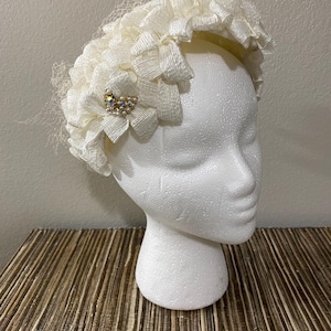 May include: A white headband with a large, ruffled flower design and a small, jeweled embellishment.