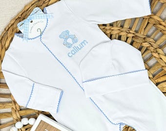 Puede incluir: Conjunto de ropa de bebé blanco con ribetes azules, con un diseño de oso de peluche y el nombre "Callum" bordado en azul. Incluye un gorro a juego y una etiqueta con un lazo azul.