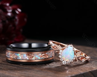May include: A pair of wedding bands. The woman's ring features a pear-shaped opal gemstone surrounded by smaller diamonds, set in a rose gold band with a delicate floral design. The man's ring is a black ceramic band with a rose gold inlay.