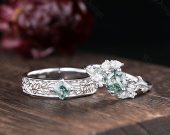 May include: A pair of silver wedding bands with green moss agate gemstones. The engagement ring features a larger moss agate stone surrounded by smaller clear diamonds and a delicate leafy design.