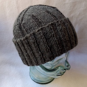 May include: A gray knitted beanie with a ribbed texture. The beanie is on a clear glass display head.