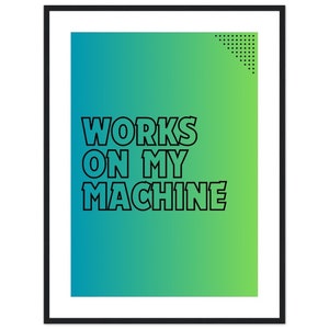 May include: A framed art print with a gradient background of teal and green. Bold black text reads "WORKS ON MY MACHINE." A small black dotted design is in the upper right corner. The frame is black.