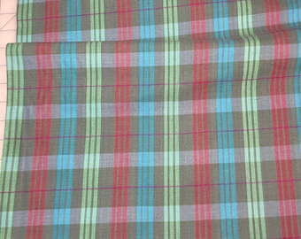 May include: Close-up of a fabric with a plaid design. The material has a grey background with red, blue, and green stripes. The fabric is folded, revealing the pattern's repeat.