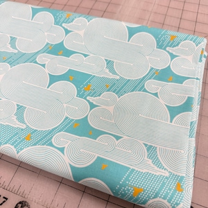 May include: Folded fabric with a repeating pattern of white, swirly clouds on a light blue background. Small yellow triangles and white dots are scattered throughout the design. The fabric is folded neatly.