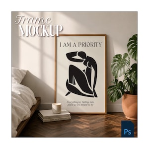 May include: A framed art print with the text "I AM A PRIORITY" and a black abstract figure. The artwork is in a wooden frame, displayed in a room setting with a bed, books, a candle, and a potted plant. The words "Everything is falling into place as it's meant to be" are also on the print.