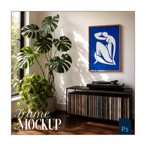 May include: A framed art print featuring a white figure on a blue background hangs on a white wall. A black record player sits on a black cabinet filled with vinyl records. A large potted plant with green leaves is in the foreground. The words "Frame MOCKUP" are at the bottom.
