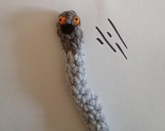 May include: A gray and white crocheted worm with orange eyes. The worm is on a white background with black lines drawn on it.