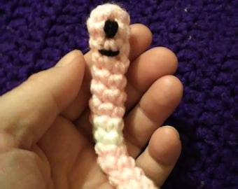 May include: A pink and white crocheted worm with a black face. The worm is about 6 inches long and has a happy expression.